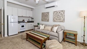 Eine moderne Küche mit weißen Schränken, einem eingebauten Ofen und einem Kühlschrank. Ein graues Sofa mit einem gewebten Ottoman und einem gestreiften Couchtisch.