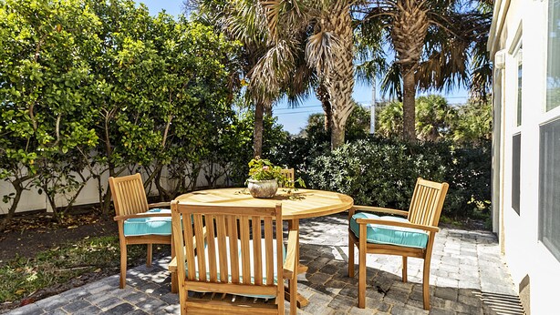 Eine Terrasse im Freien mit einem runden Holztisch und vier Holzstühlen mit blauen Kissen.