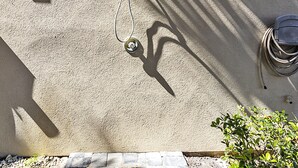 Ein Gebäudefassadenn mit einer an einer Wand aufgewickelten Metallschlauch, einem vergitterten Fenster und einer kleinen Pflanze am Fuße.