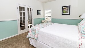 Ein Schlafzimmer mit einem Bett, einem Deckenventilator, einer Tür mit Glasfeldern und einem Fenster mit Jalousien.
