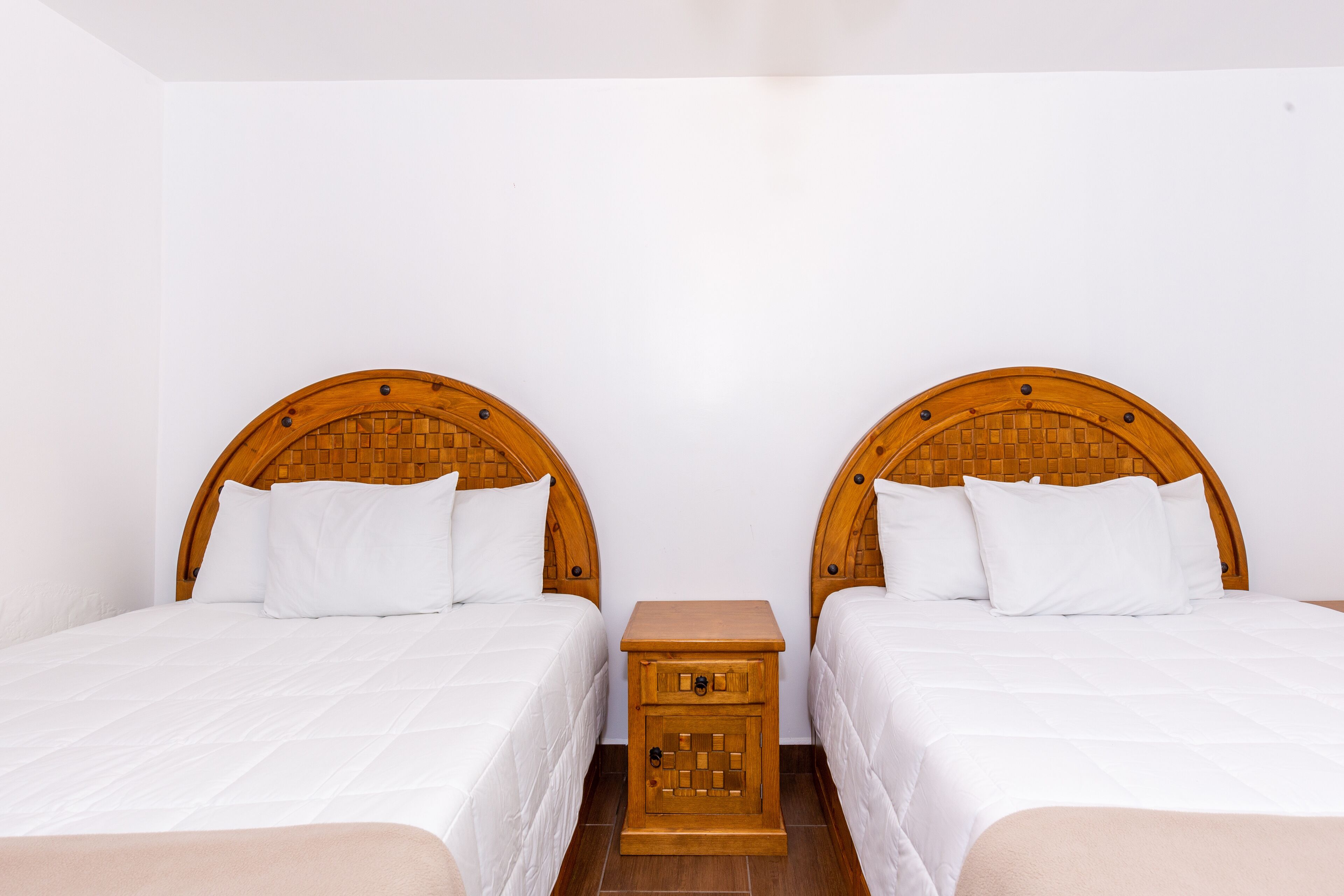 Ein Zimmer mit zwei Einzelbetten, jeweils mit einem hölzernen Kopfteil, einem kleinen Nachttisch dazwischen und weißer Bettwäsche.
