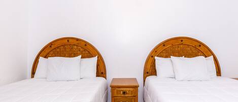 Ein Zimmer mit zwei Einzelbetten, jeweils mit einem hölzernen Kopfteil, einem kleinen Nachttisch dazwischen und weißer Bettwäsche.