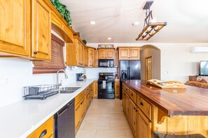 Una cocina con armarios de madera, un lavamanos de acero inoxidable, un microondas, un refrigerador y una encimera de madera.