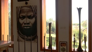 Una habitación con un cuadro grande, un jarrón y una escultura cerca de una ventana.