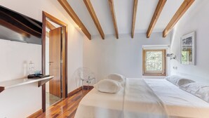 Une chambre avec un plafond en bois, un lit avec une literie blanche, une chaise et une fenêtre donnant sur un paysage verdoyant.