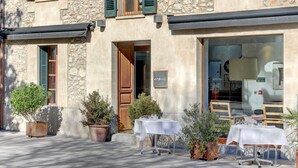 Un bâtiment en pierre doté d’un espace café avec des tables en plein air et des plantes en pot.