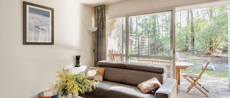 A modern living room with a sofa, a coffee table, and a large window offering a view of the outdoors.