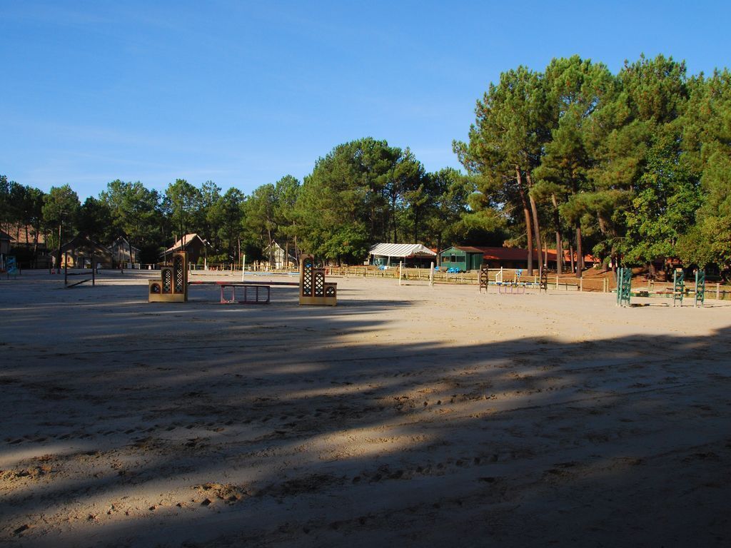 A spacious outdoor area with a sandy surface, surrounded by trees and buildings.