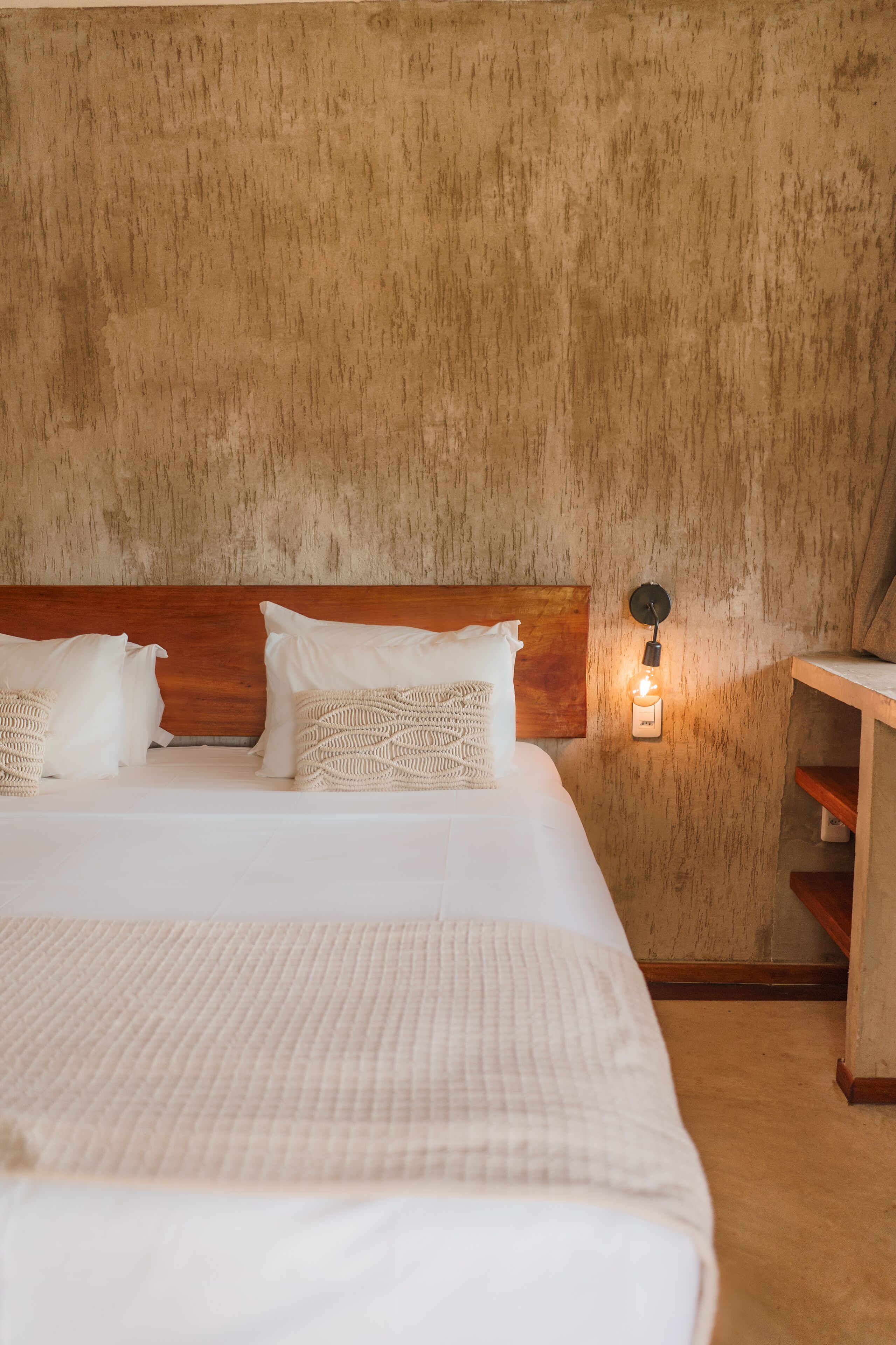 Een bed met een houten hoofdbord, witte beddengoed en een wandlamp.
