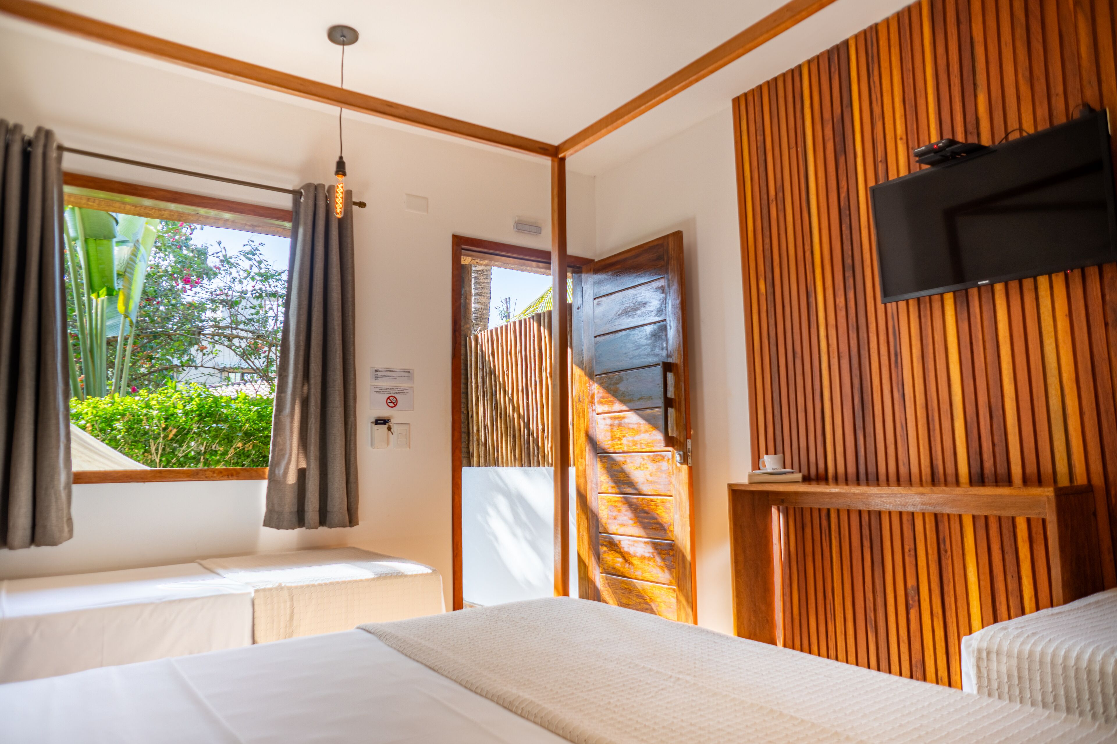 A hotel room with two beds, a TV mounted on the wall, and a window with curtains.