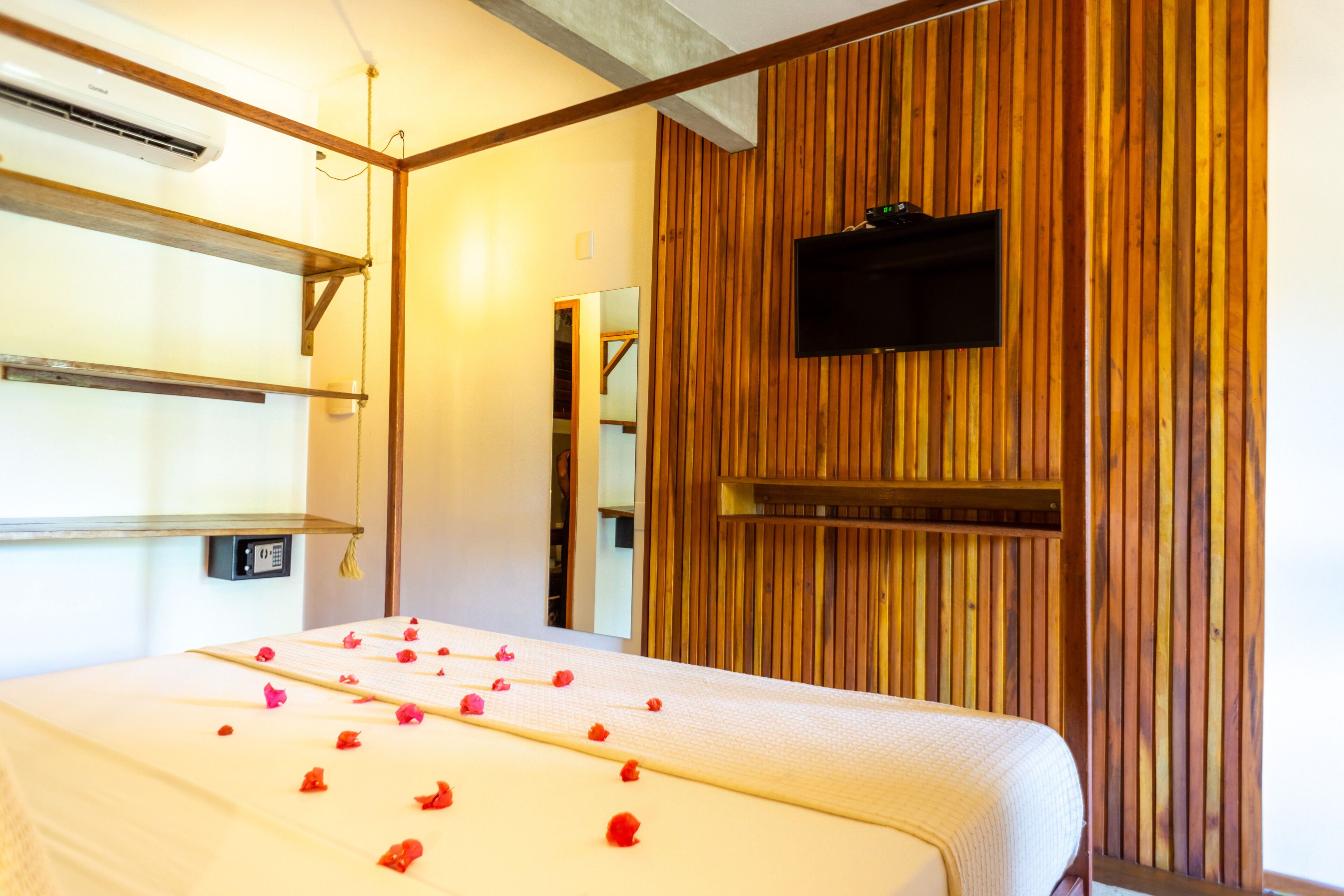 A hotel room with a bed, wooden panel walls, a mounted TV, and a bedside table with a lamp.
