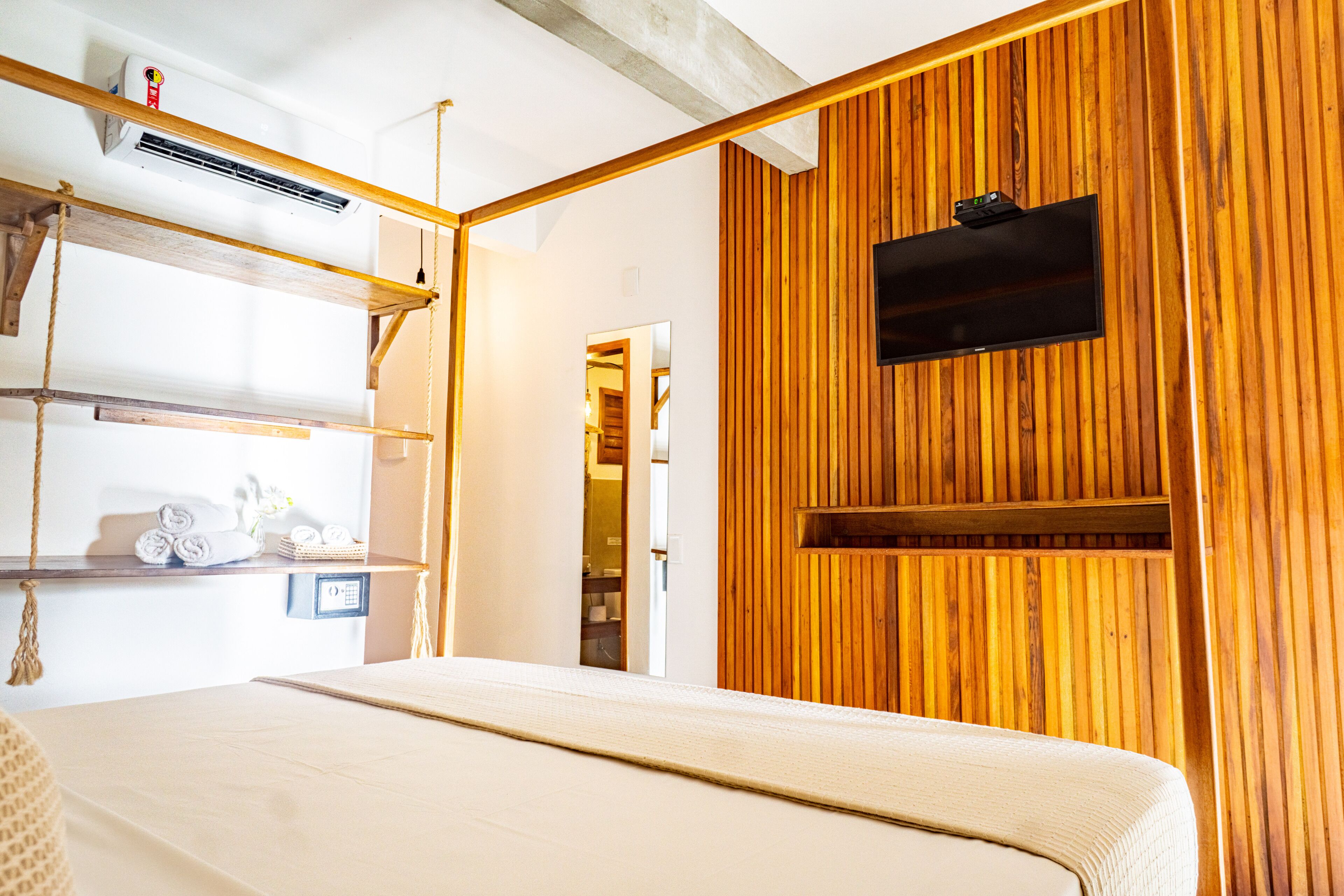 Ein Hotelzimmer mit Holzwand, einem an der Wand befestigten Fernseher, einem Bett mit weißer Bettdecke und einem Regal mit Handtüchern.