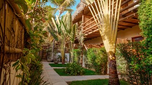 A tropical garden with a pathway leading to a wooden building with a thatched roof. - Casa Valentini Pousada (Jijoca de Jericoacoara)