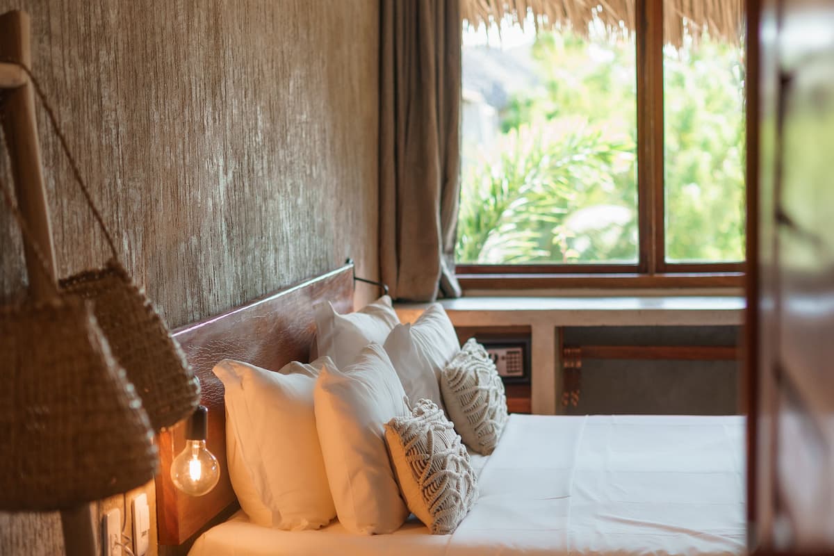 Une chambre à coucher avec un lit, une petite table, une lampe et une fenêtre avec des rideaux.