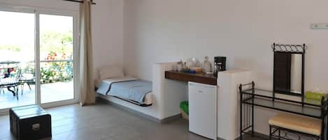 Una habitación funcional con cama, kitchenette pequeña, comedor y puerta corrediza al exterior.