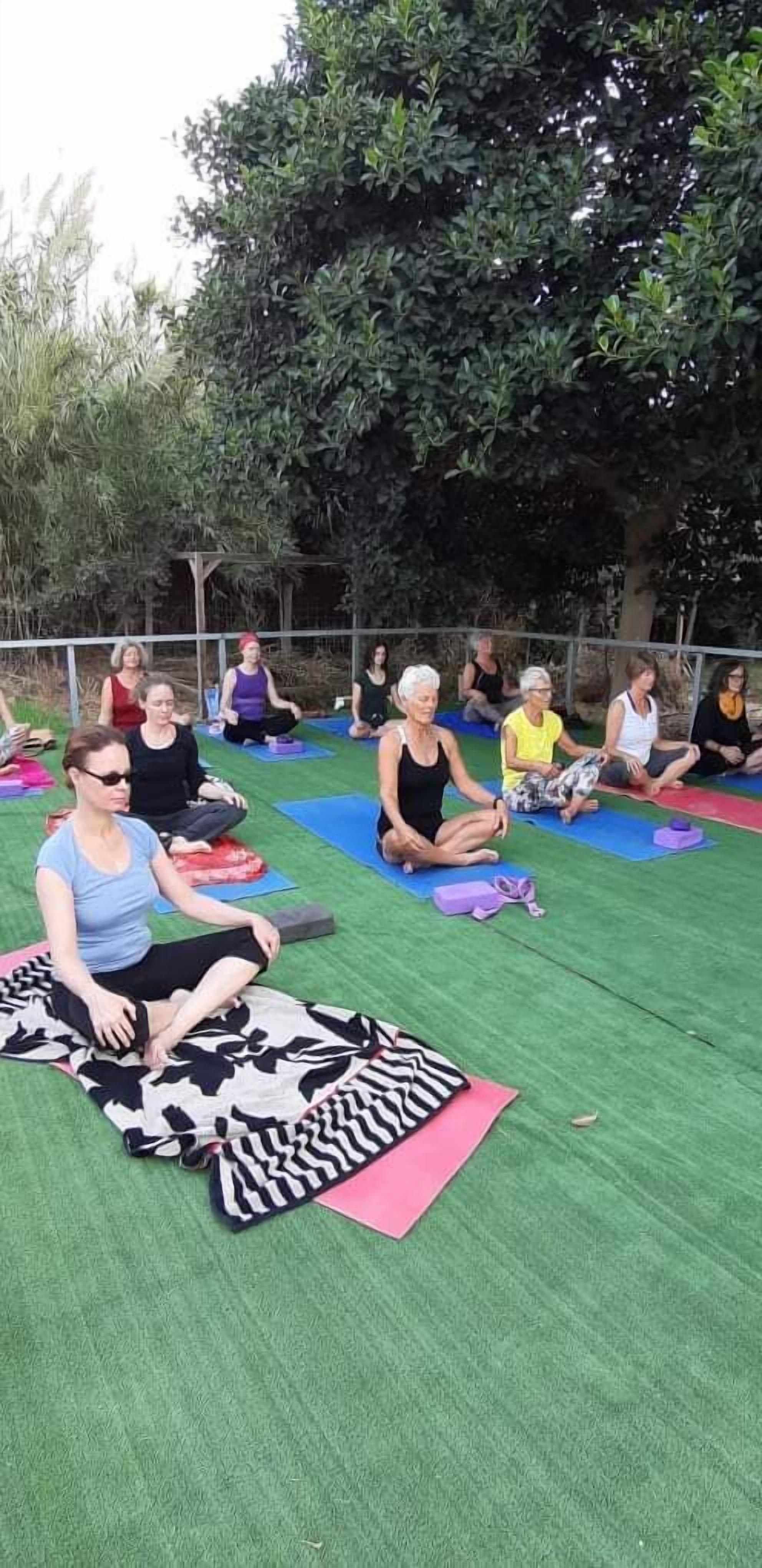 A group of people sitting on mats outdoors, possibly for a yoga or meditation session.