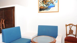 Ein Zimmer mit einem blauen Sofa, einem Holzstuhl und einem Glastisch mit einem Buch.