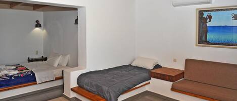 Una habitación compacta con una cama, un sofá, una mesita y un cuadro en la pared.