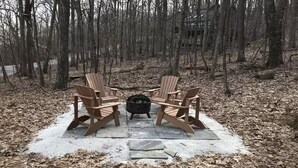 Ein hölzerner Adirondack-Stuhl auf einer Steinterrasse, umgeben von einem Wald.
