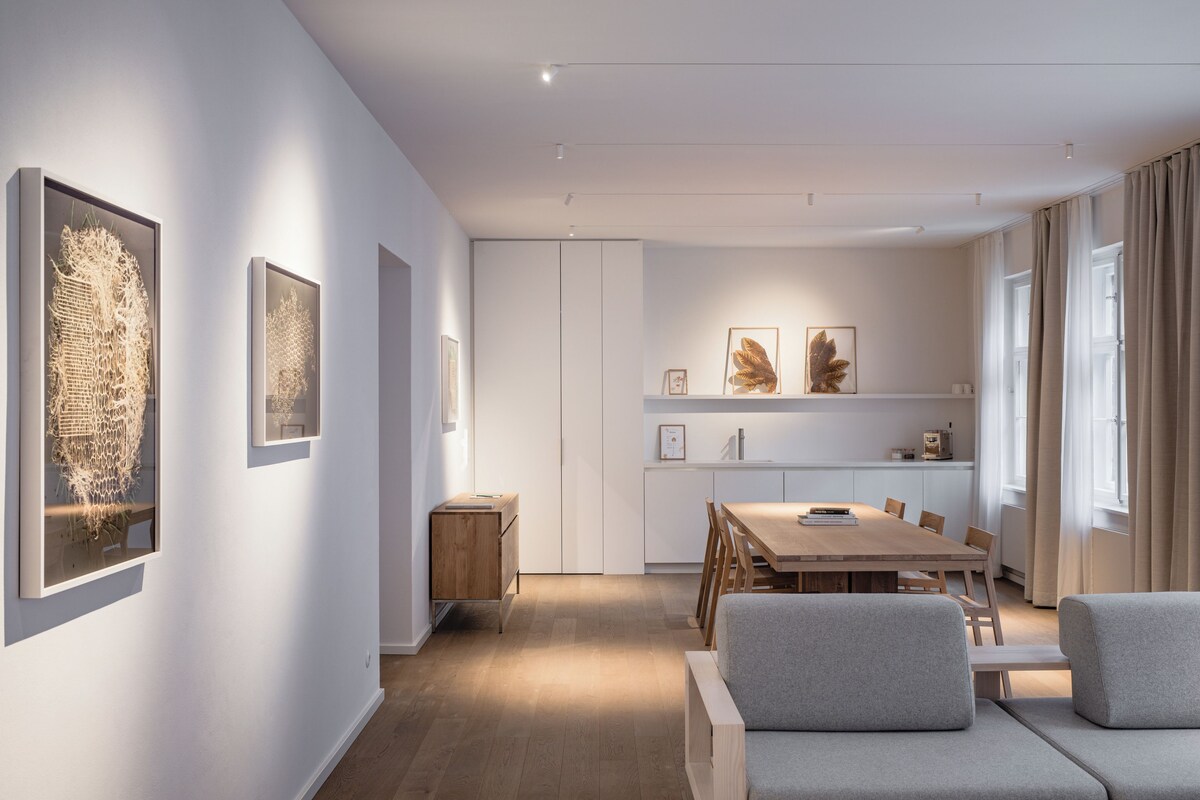 A modern dining area with a wooden table and chairs, a sofa, and framed artwork on the walls.