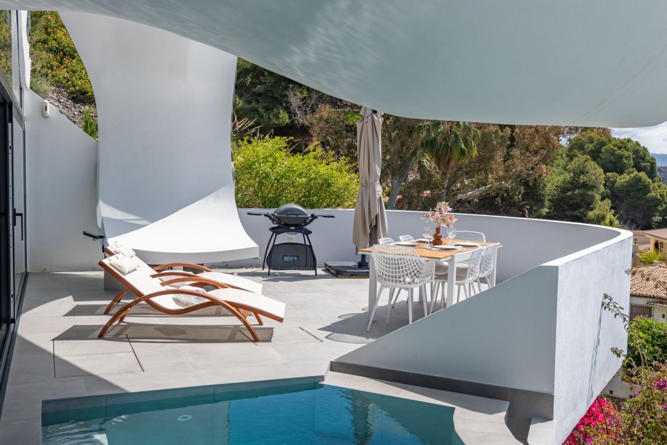 A modern outdoor pool area with lounge chairs, a barbecue grill, and a dining table with chairs.