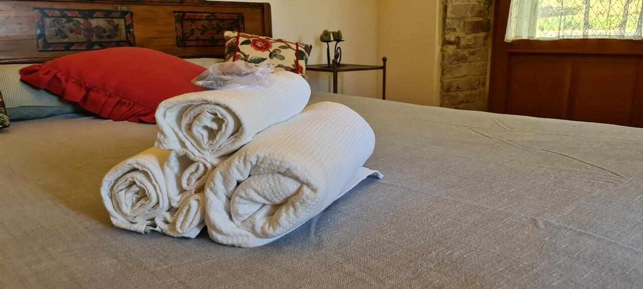 A neatly made bed with rolled towels and a red pillow.