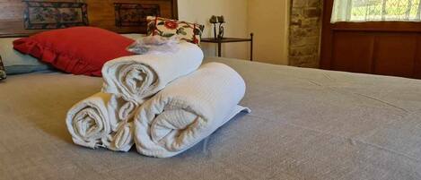 A neatly made bed with rolled towels and a red pillow.