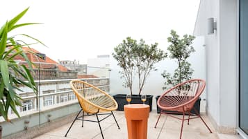 A balcony with two wicker chairs, a potted plant, and a small table with two glasses.
