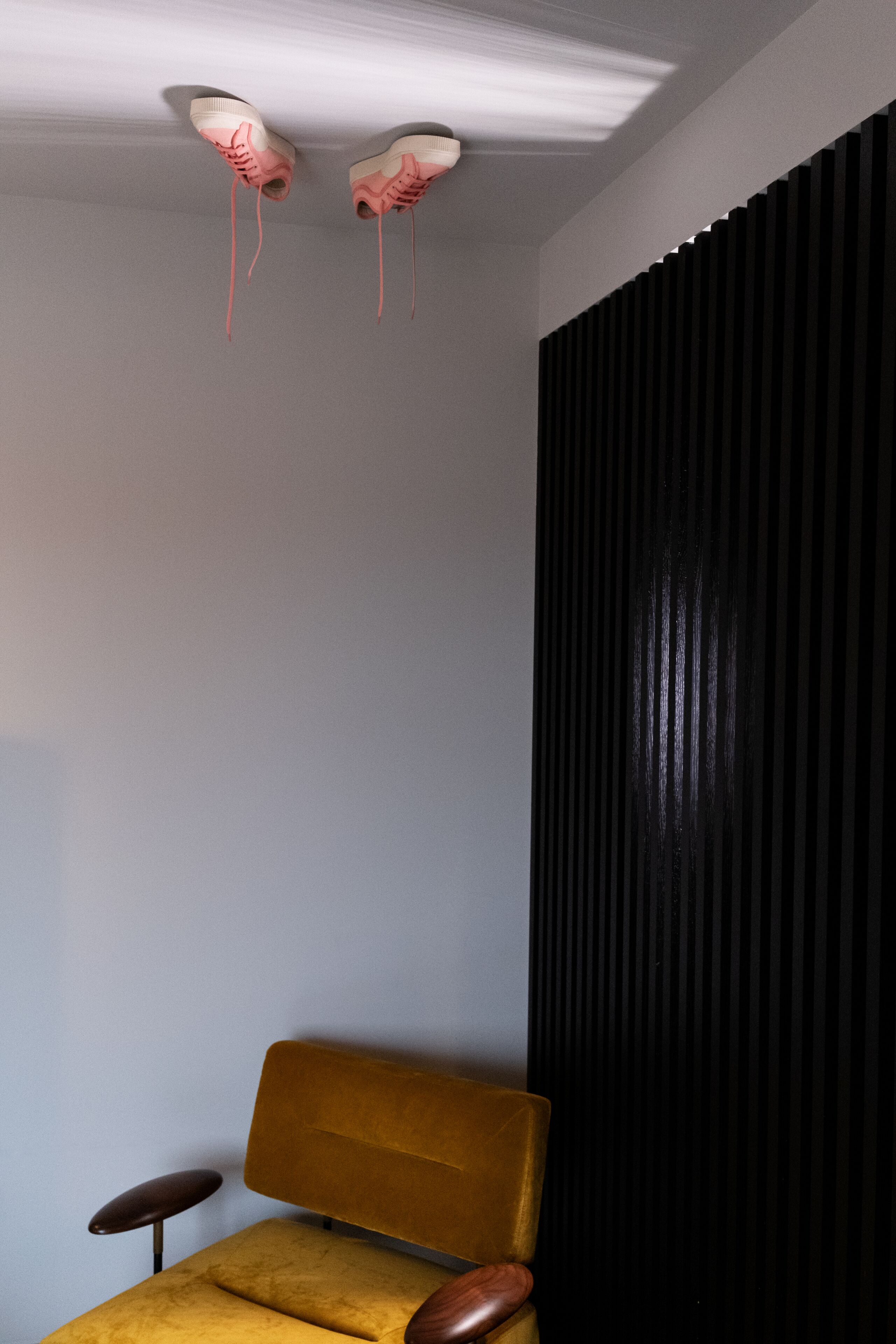 A room with a yellow armchair, a black acoustic panel, and a ceiling light fixture.