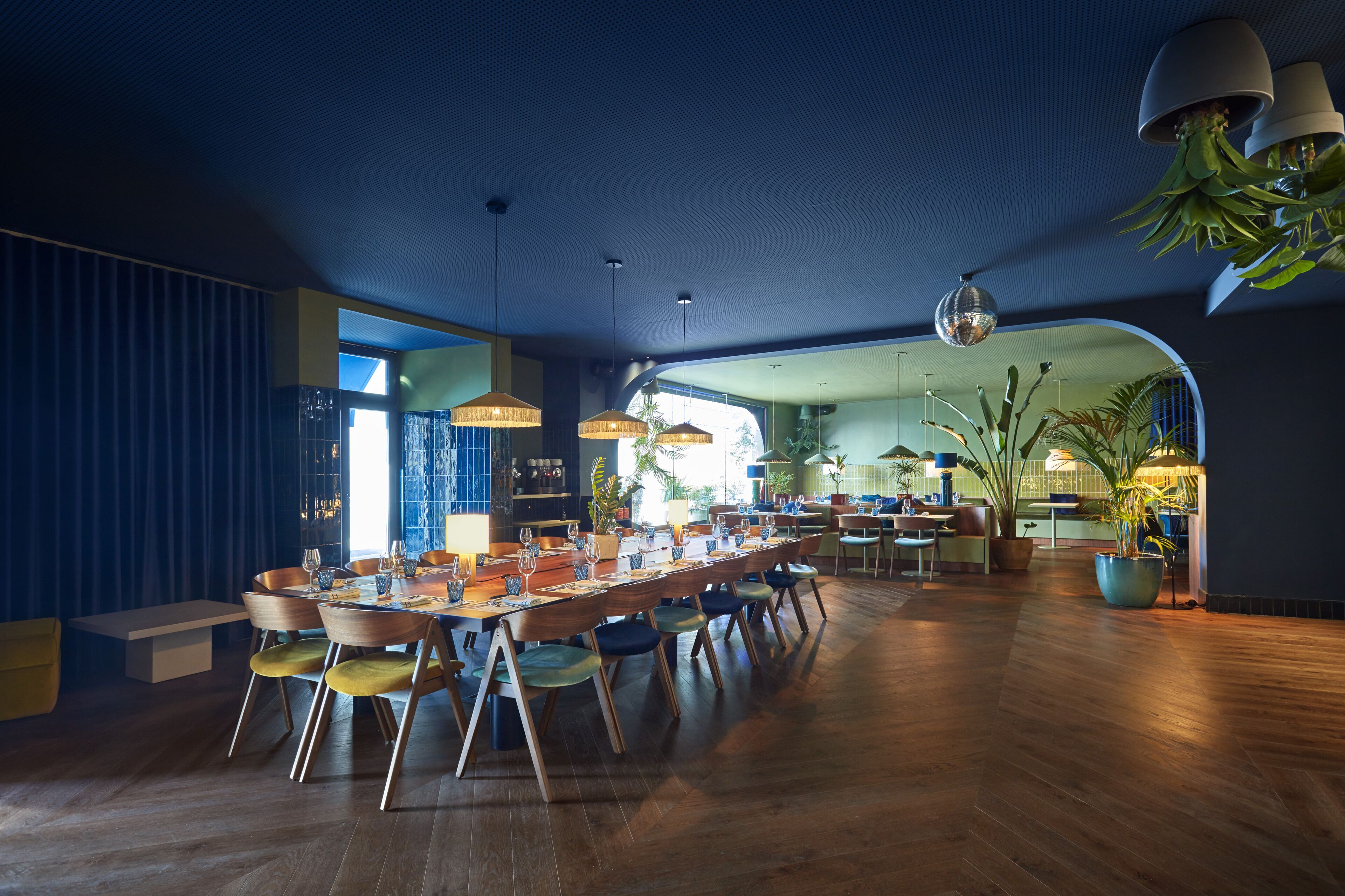 A modern dining area with a long wooden table, multiple chairs, and hanging pendant lights.