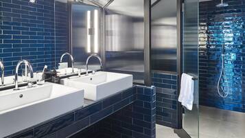 A modern bathroom with two sinks, a glass shower enclosure, and blue-tiled walls.