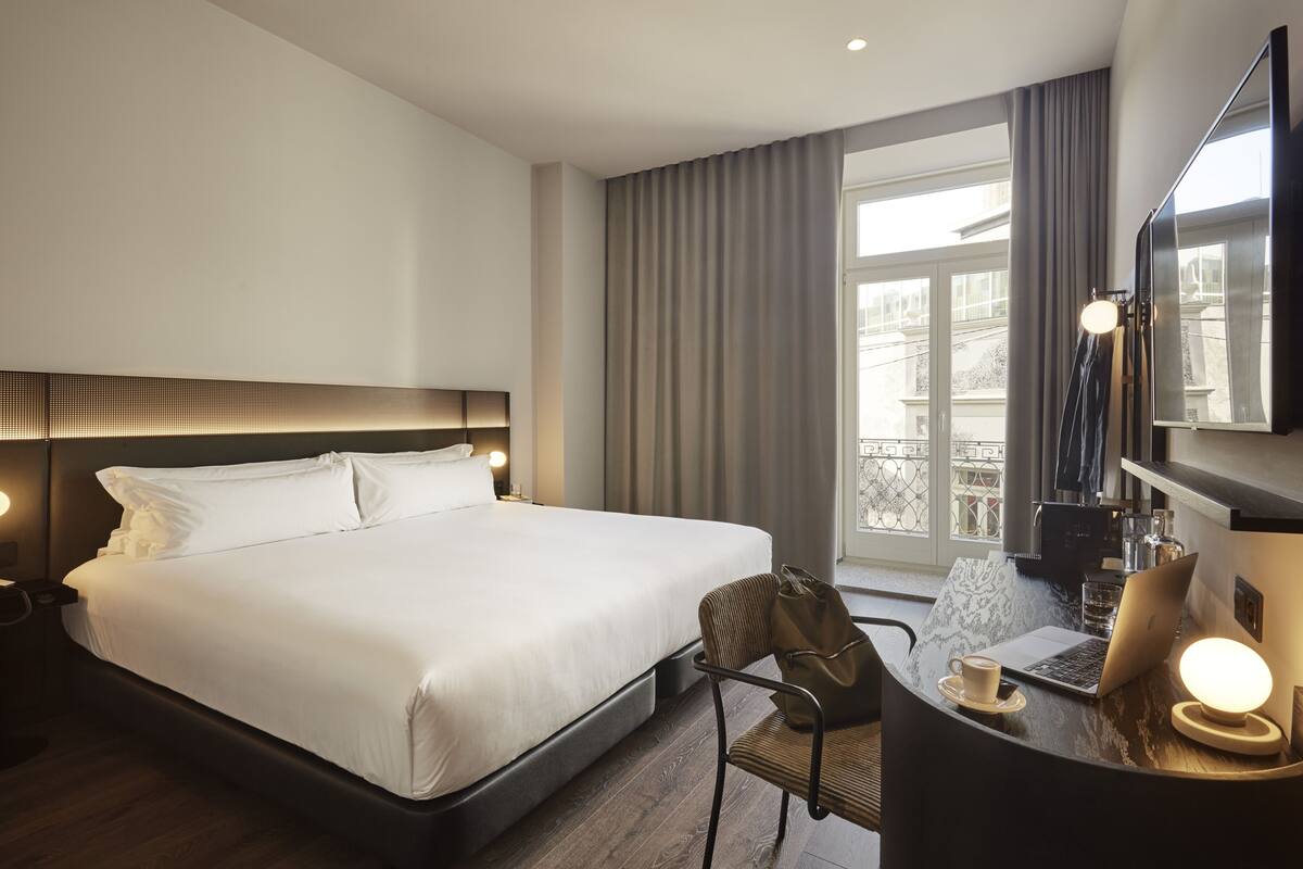 A hotel room with a large bed, a desk with a laptop, a chair, and a coffee cup.