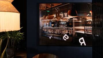 A bar area with shelves of bottles, a large hanging light fixture, and a potted plant.
