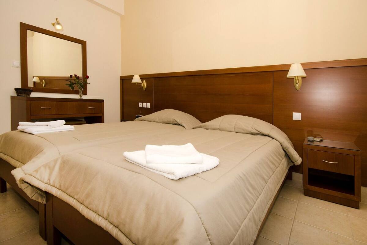 Habitación de hotel con una cama grande, cabecera de madera, mesita de noche, espejo y lámpara.