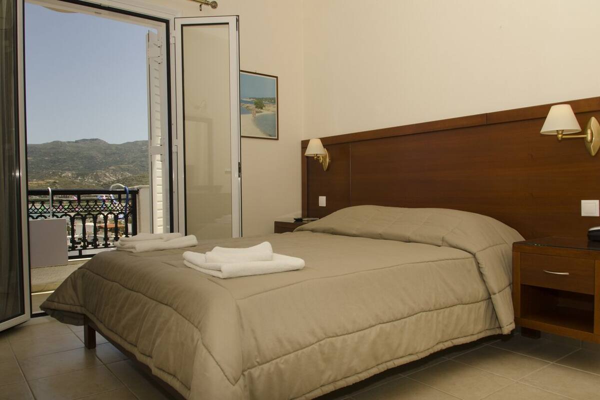 Un dormitorio con una cama grande, un cabecero de madera, lámparas de noche, una mesita de noche y vistas al exterior a través de una puerta corredera.