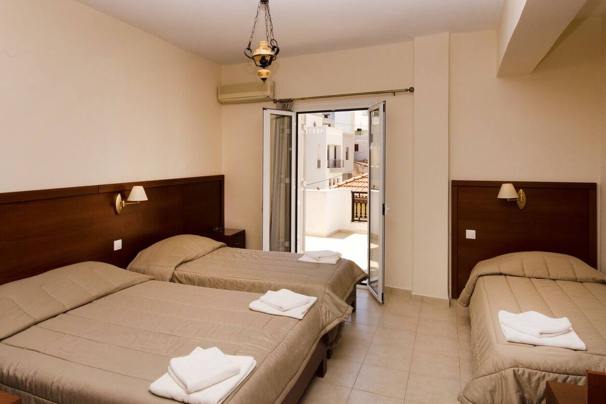 Habitación de hotel con dos camas, cada una con cabecero de madera y lámpara de noche. Una puerta corrediza de vidrio da a un área exterior.