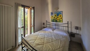 Un dormitorio con cama, ventana con cortinas, un cuadro en la pared y techo con vigas de madera.
