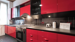 A modern kitchen with red cabinetry, a gas stove, a kettle, and a coffee maker. - Italianway - Massarani 5 (Milan)