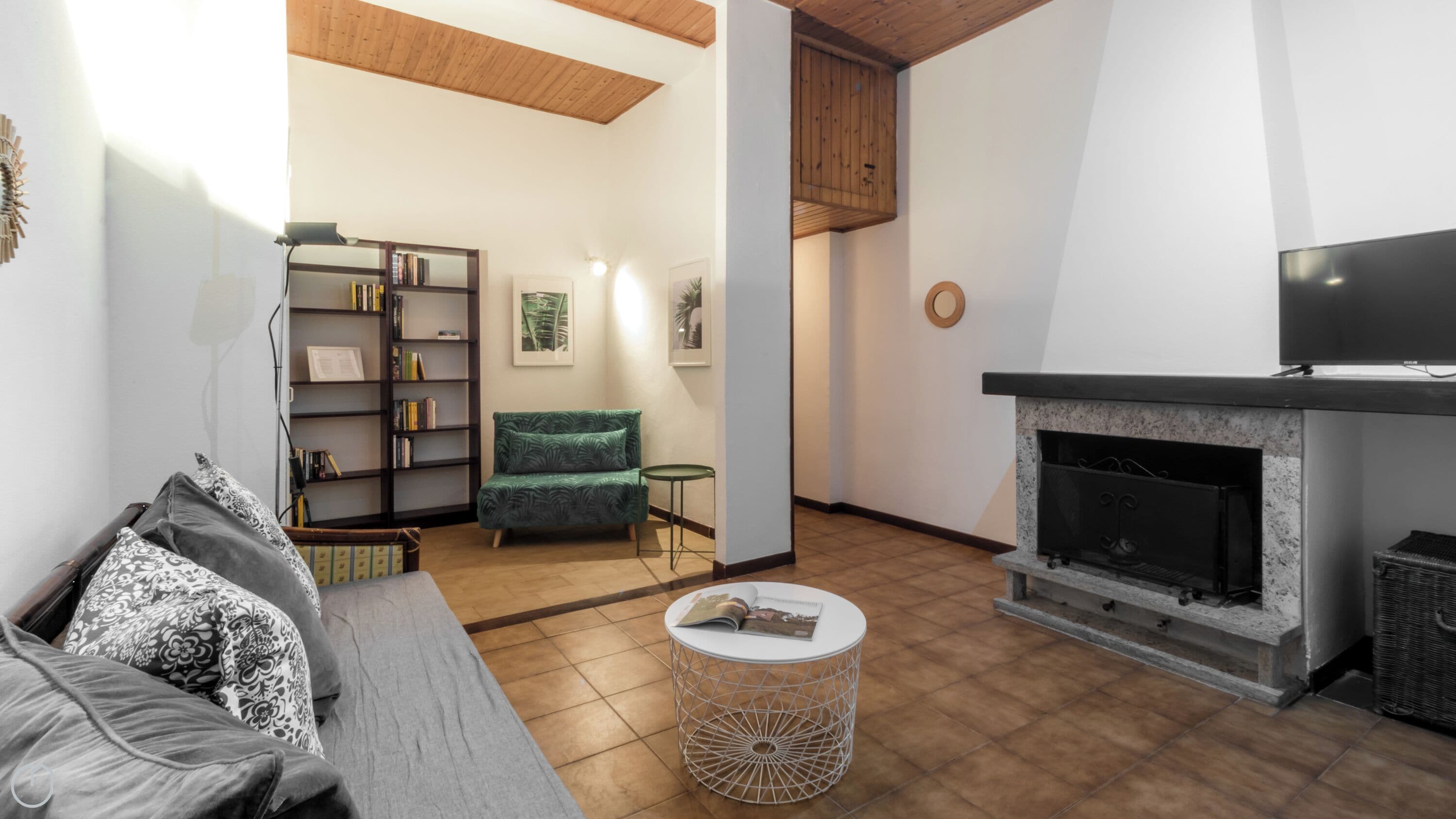 A living room with a fireplace, a sofa, a green armchair, a bookshelf, and a round coffee table.