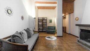 A living room with a sofa, a round coffee table, a bookshelf, a green armchair, and a fireplace. - Italianway - Massarani 5 (Milan)