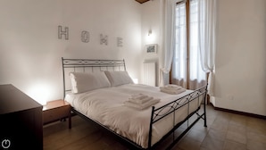 A neatly made bed with white linens and towels, a wooden nightstand, and a wall with the letters "HOME" spelled out. - Italianway - Massarani 5 (Milan)