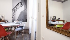 A dining area with a white table set for four, surrounded by chairs. A large mirror with a gold frame reflects the room. - Italianway - Piero Della Francesca 84 (Milan)
