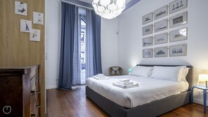 A modern bedroom with a large bed, a wooden dresser, a chandelier, and a cityscape wall art. - Italianway - Piero Della Francesca 84 (Milan)