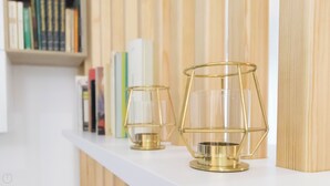 Deux photophores en verre sont posés sur une étagère blanche, avec un fond en bois et une bibliothèque remplie de livres.