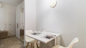 Un coin repas moderne avec une table blanche dressée pour deux personnes, comprenant des assiettes, des verres et des couverts.