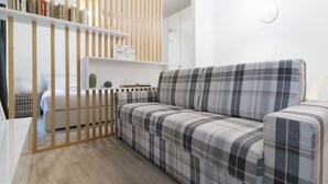Un salon moderne avec un canapé à carreaux, une bibliothèque en bois et un petit cactus posé sur une console blanche.