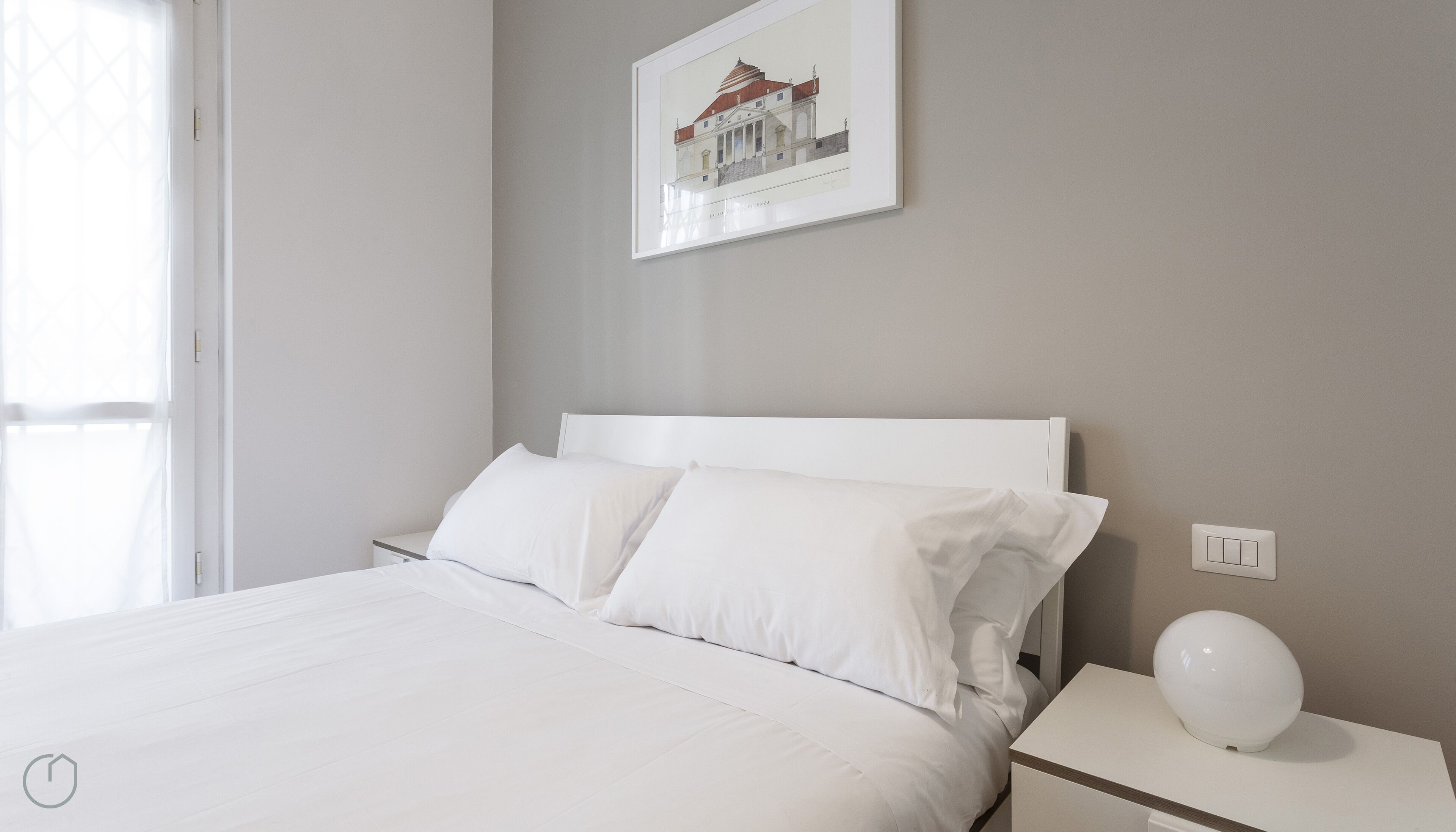 A neatly made bed with white linens in a room with a light grey wall.