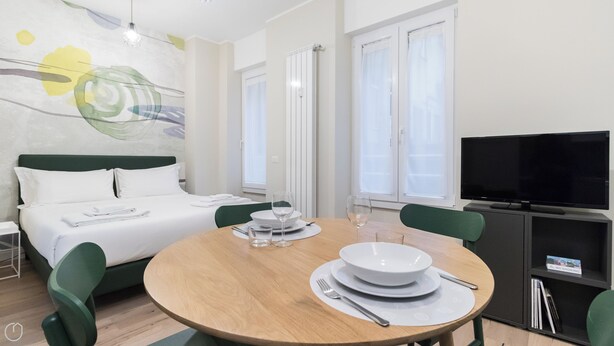 A hotel room with a bed, a dining table with chairs, a television, and a large window. - Italianway - Garibaldi 104 A (Milan)