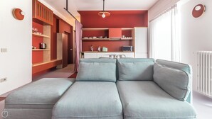 A modern living room with a sectional sofa, a kitchen area with red cabinets, and a dining table. - Italianway - Bassini 31 (Milan)