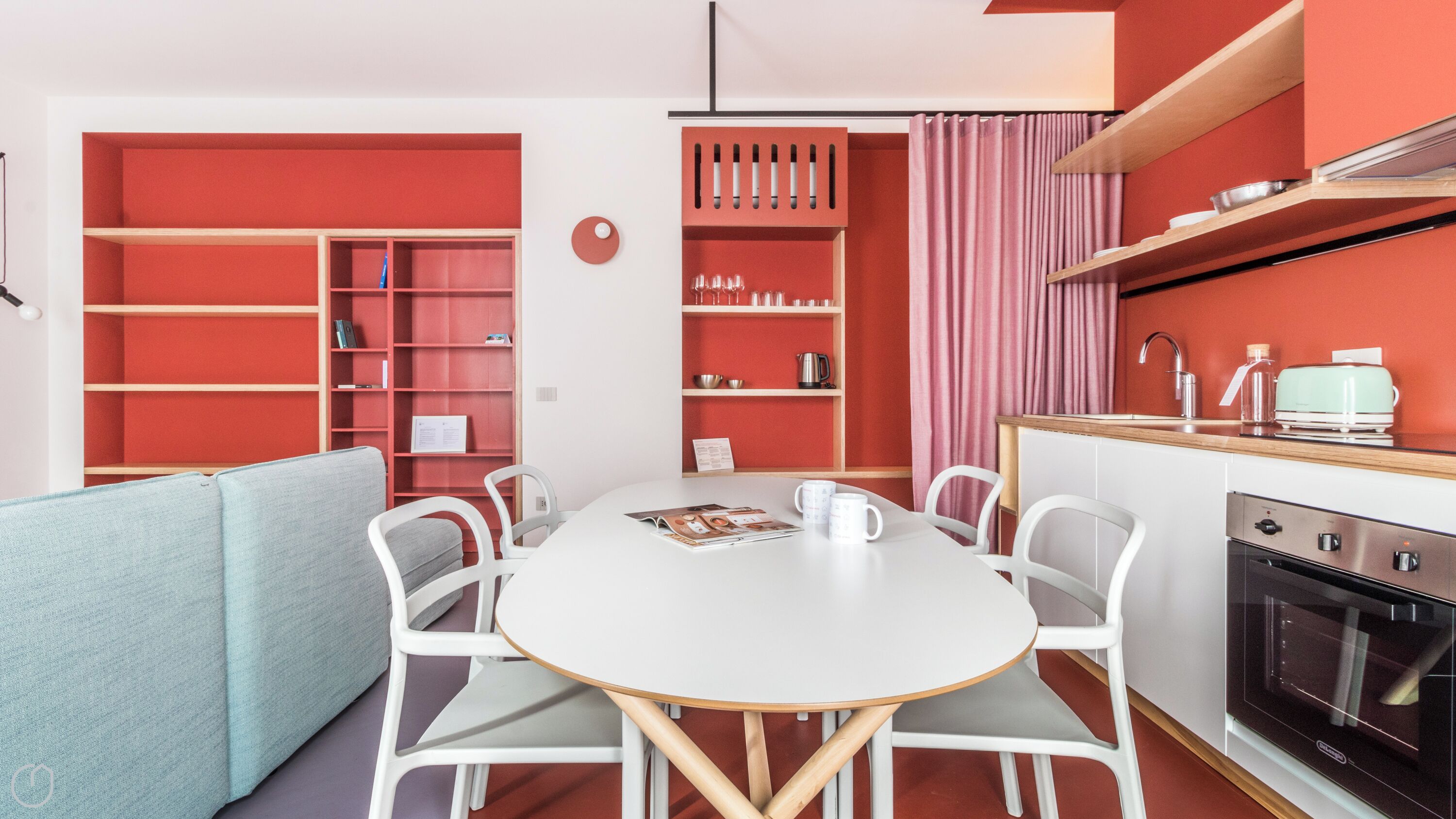 A compact kitchen with a dining area, featuring a round table, white chairs, and a built-in oven.